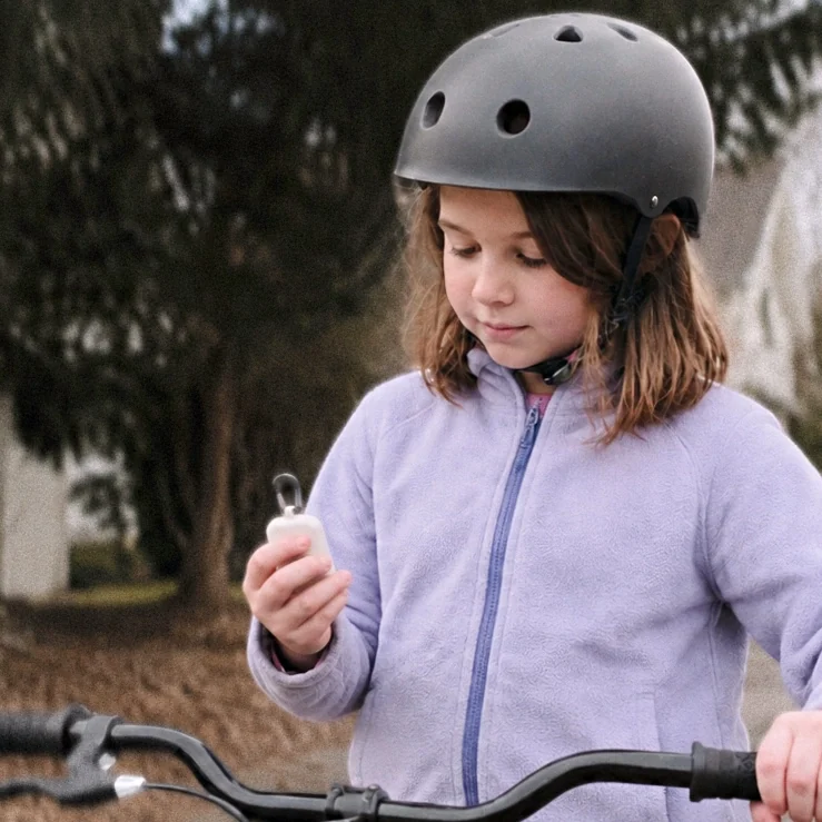 A child in a bike helmet holding ReadyChime beside a bicycle